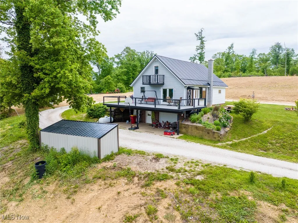 Back of house featuring dirt driveway, a deck, metal roof, a chimney, and a standing seam roof