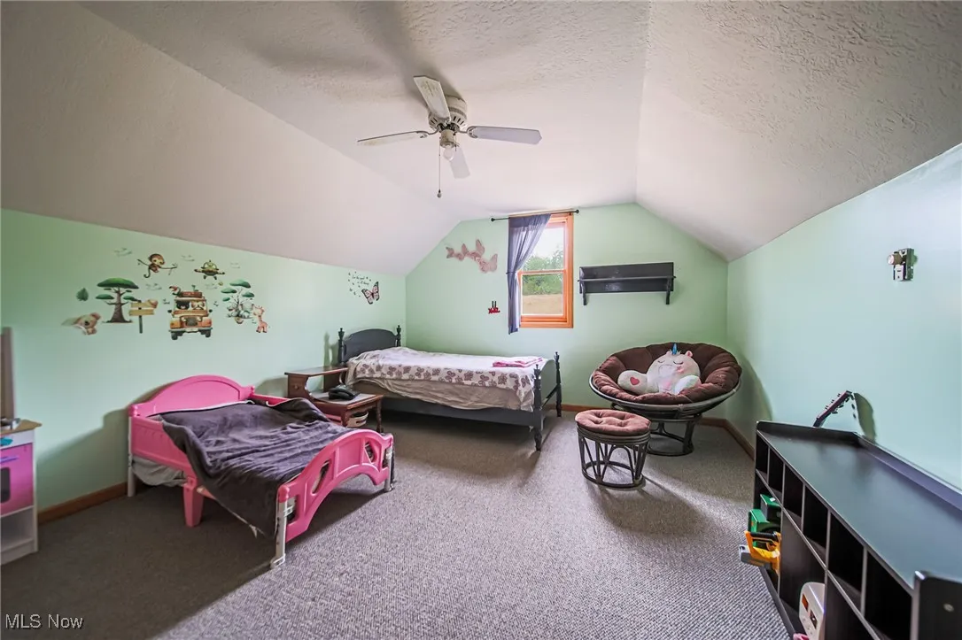 Carpeted bedroom with ceiling fan, vaulted ceiling, a textured ceiling, and baseboards
