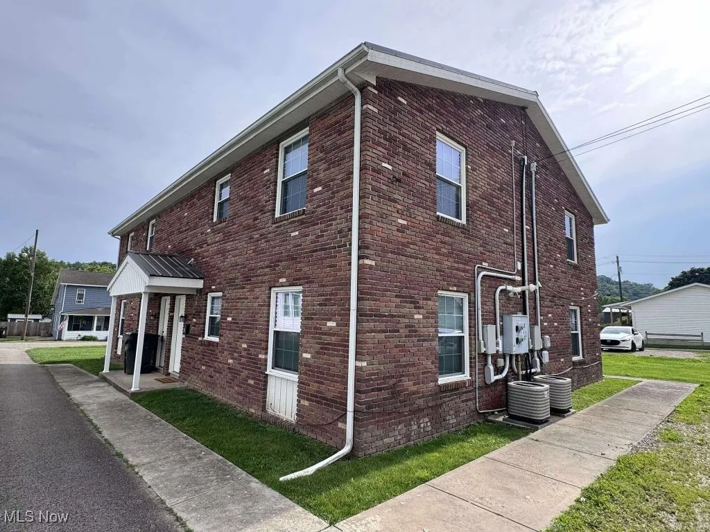 View of side of property with brick siding, a yard, and cooling unit
