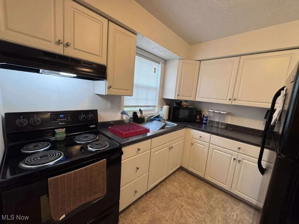 Kitchen with black appliances, exhaust hood, a textured ceiling, white cabinets, and dark countertops