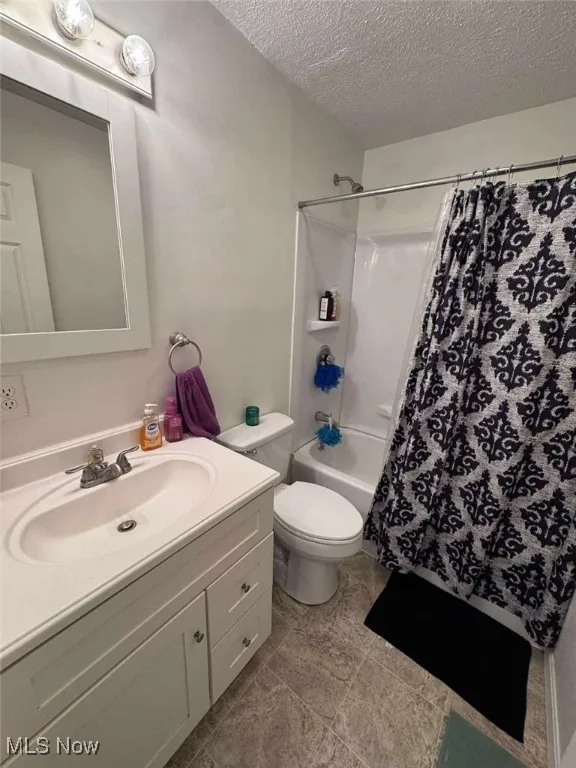 Bathroom featuring a textured ceiling, vanity, toilet, and shower / bath combo