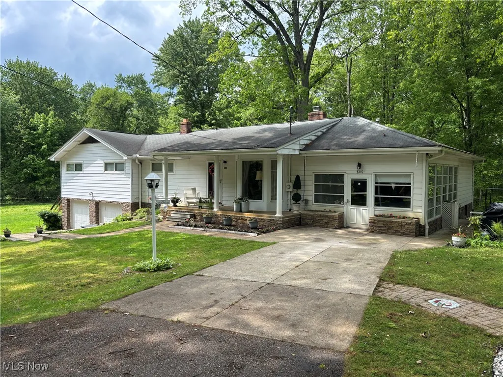 View of front of house featuring a chimney, concrete driveway, a porch, a front lawn, and an attached garage