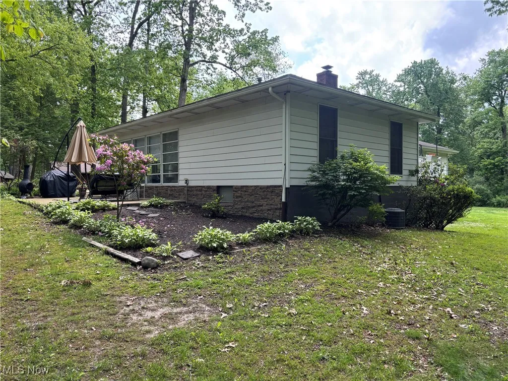 View of side of home featuring a chimney, a lawn, and central air condition unit