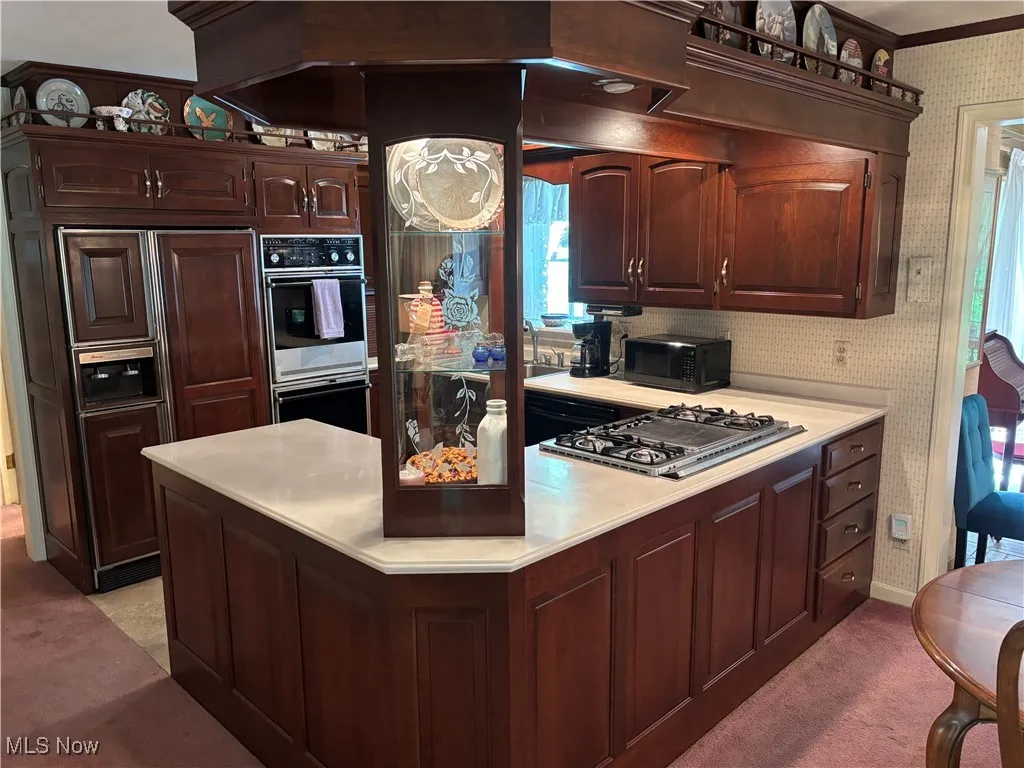 Kitchen with wallpapered walls, stainless steel gas stovetop, light countertops, double oven, and black microwave