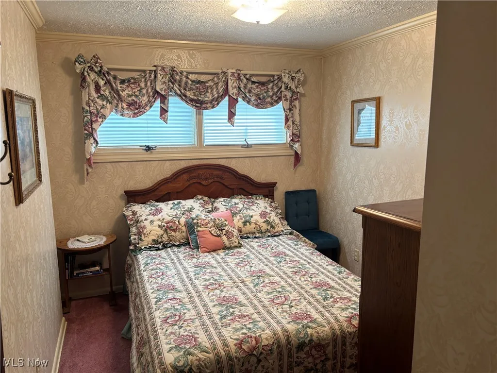 Carpeted bedroom with a textured ceiling, multiple windows, wallpapered walls, and crown molding