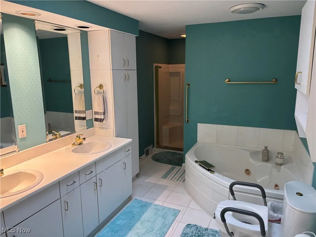 Full bathroom featuring a whirlpool tub, double vanity, a shower stall, and tile patterned floors