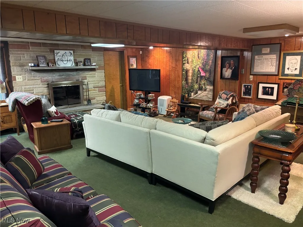 Carpeted living area with wood walls and a stone fireplace