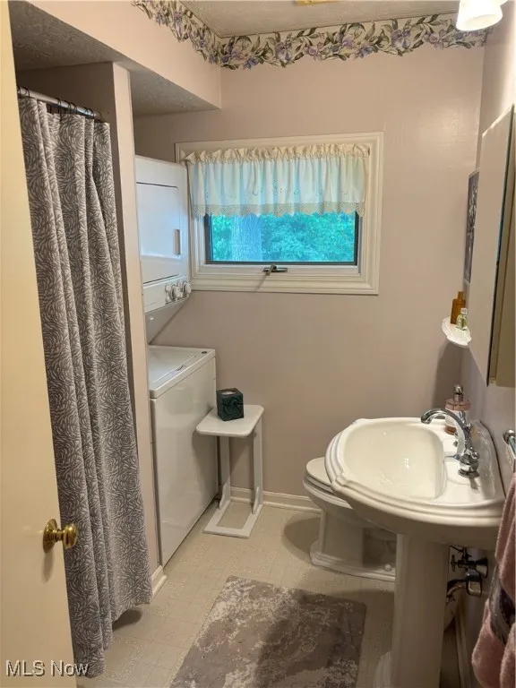 Bathroom featuring stacked washing machine and dryer, toilet, curtained shower, and baseboards