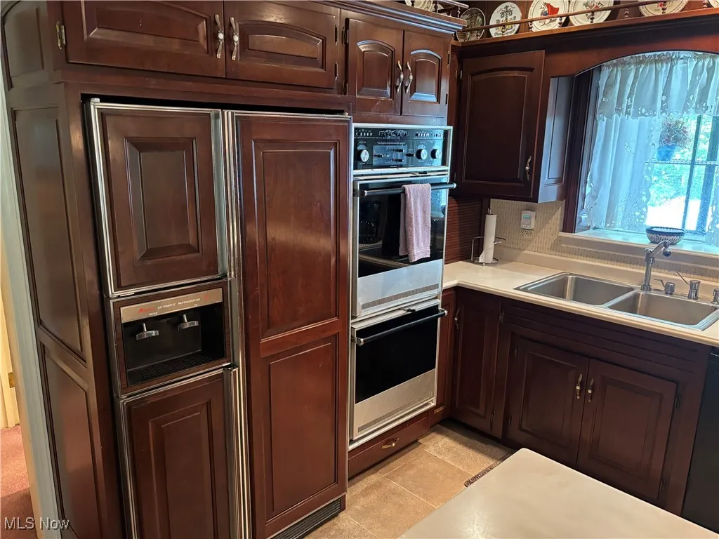 Kitchen featuring a sink, double wall oven, light countertops, dark brown cabinets, and light tile patterned floors