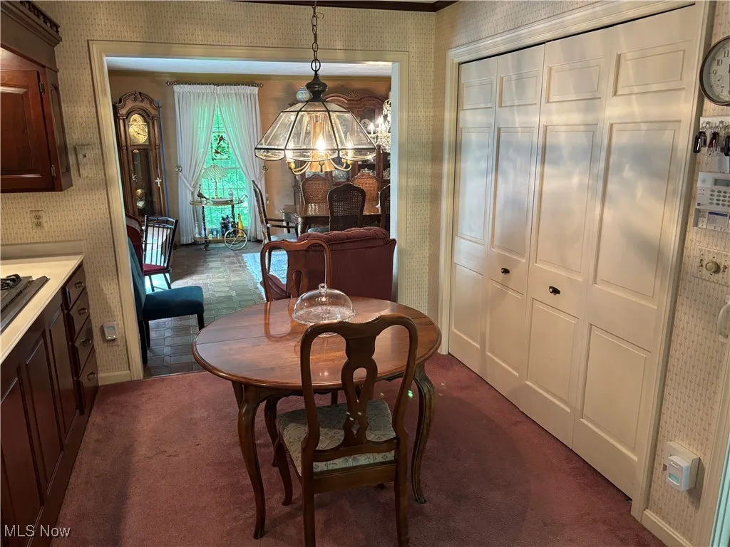 Dining area with wallpapered walls, dark colored carpet, a chandelier, and baseboards