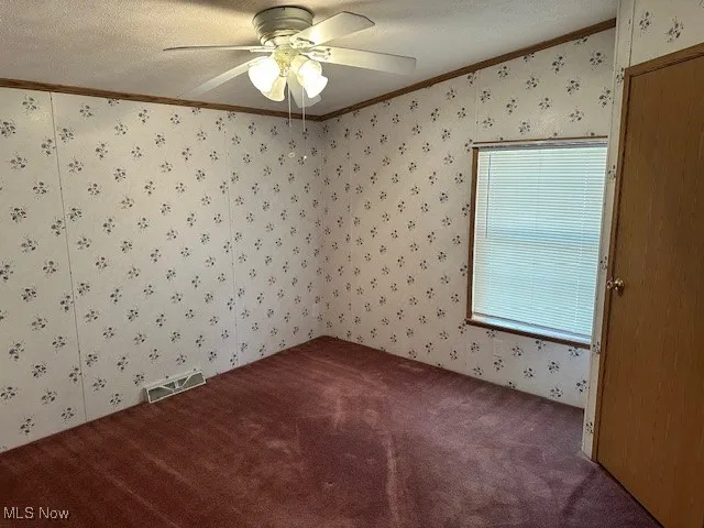 Bedroom featuring wallpapered walls, ornamental molding, carpet, a ceiling fan, and a textured ceiling