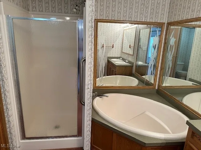 Bathroom featuring a double vanity, a shower stall, toilet, and a bath