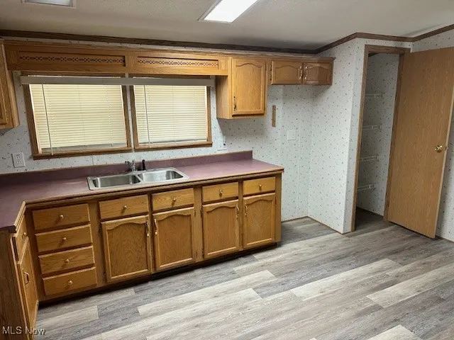 Kitchen featuring a sink, ornamental molding, light wood finished floors, and brown cabinetry