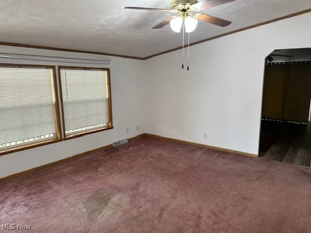 Spacious family room featuring dark colored carpet, ornamental molding, a ceiling fan, a textured ceiling, and baseboards
