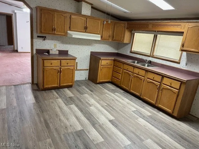 Kitchen with a sink, lofted ceiling, under cabinet range hood, brown cabinets, and light wood-style flooring