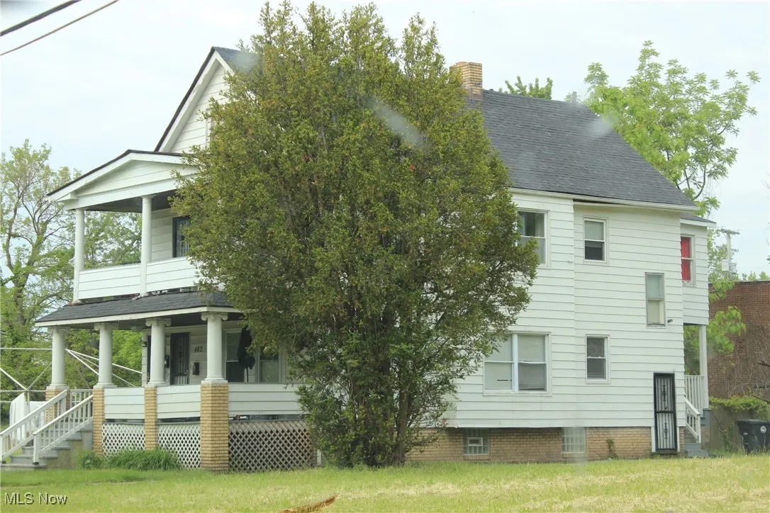 View of side of home featuring covered porch, a yard, a shingled roof, and a chimney
