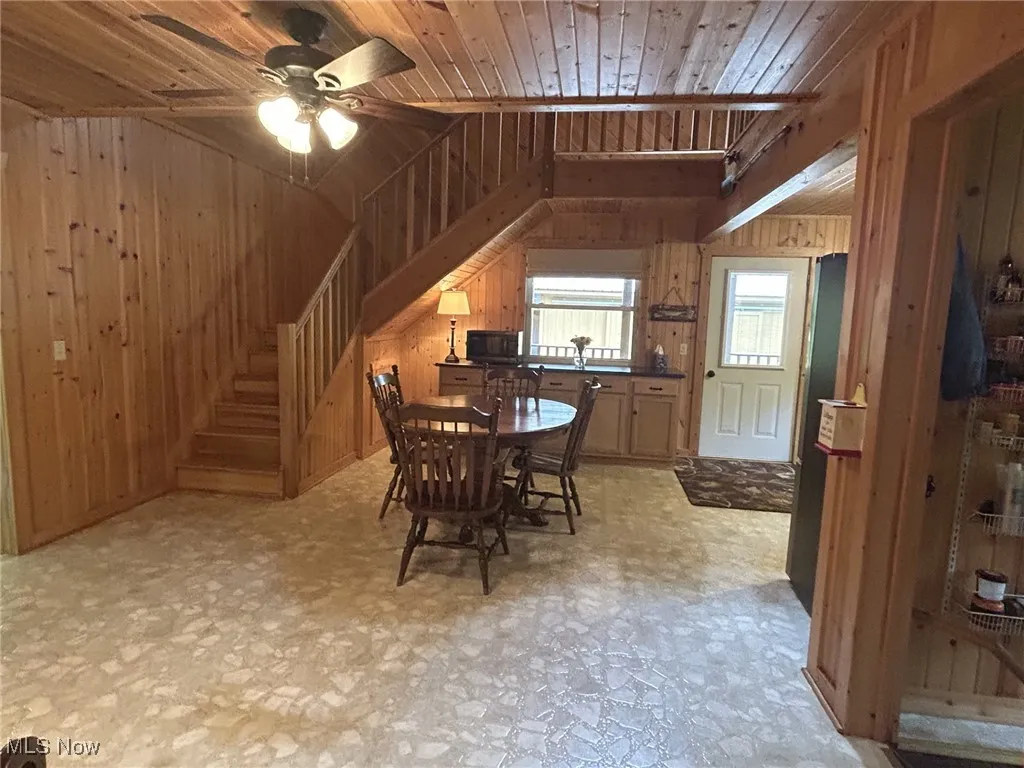 Dining room with wood walls, a ceiling fan, wood ceiling, lofted ceiling, and light floors