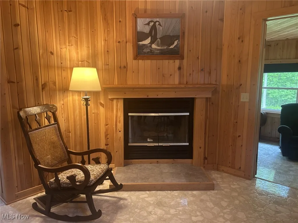 Living area featuring tile patterned floors, wooden walls, and a glass covered fireplace