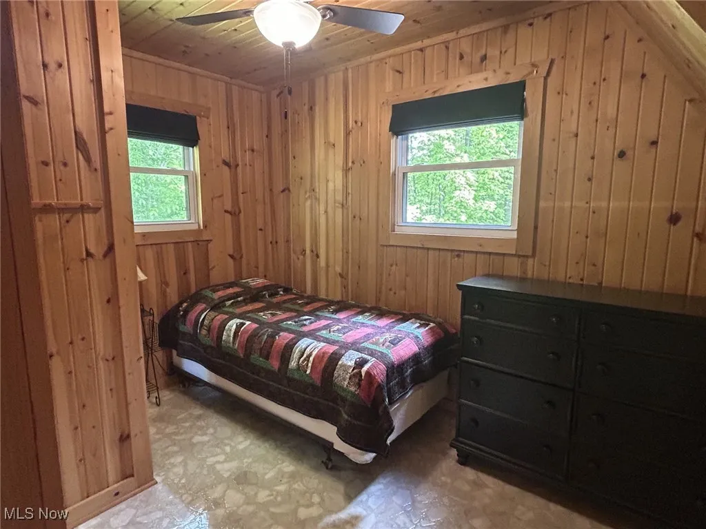 Bedroom with wood walls, tile patterned floors, wooden ceiling, and a ceiling fan