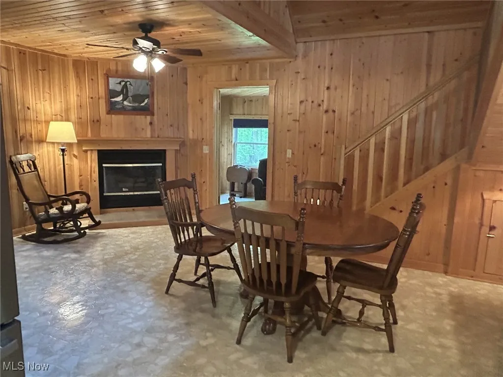 Dining space with wood walls, wooden ceiling, ceiling fan, stairs, and a glass covered fireplace