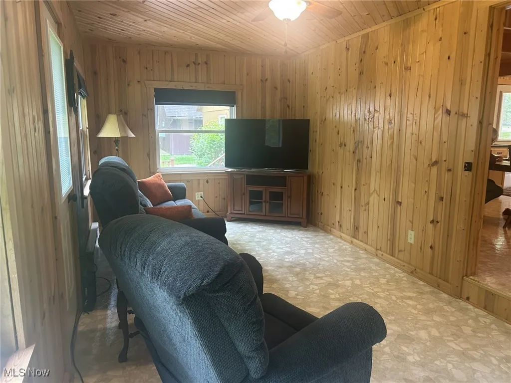 Living room featuring wood walls, wood ceiling, healthy amount of natural light, ceiling fan, and baseboards