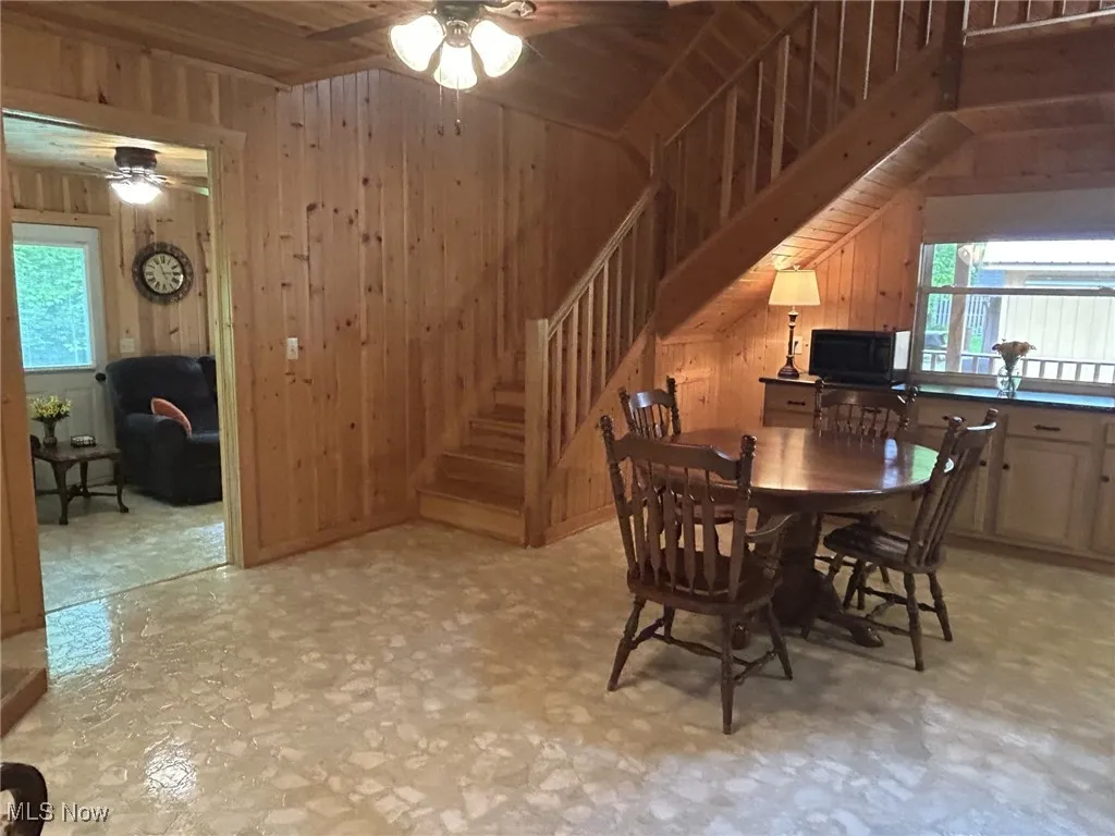 Dining space featuring ceiling fan, plenty of natural light, wooden walls, stairway, and lofted ceiling