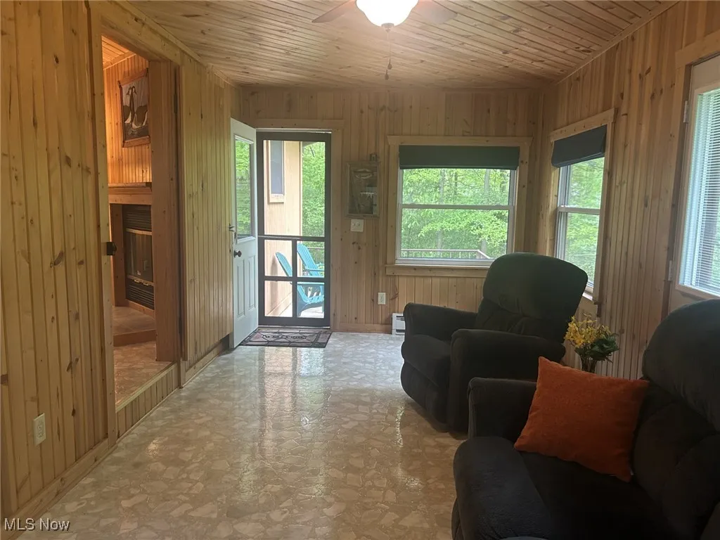 Living room featuring wooden walls, a ceiling fan, wood ceiling, and baseboards
