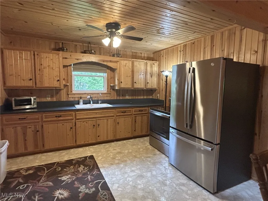 Kitchen with appliances with stainless steel finishes, a sink, dark countertops, wood walls, and wooden ceiling