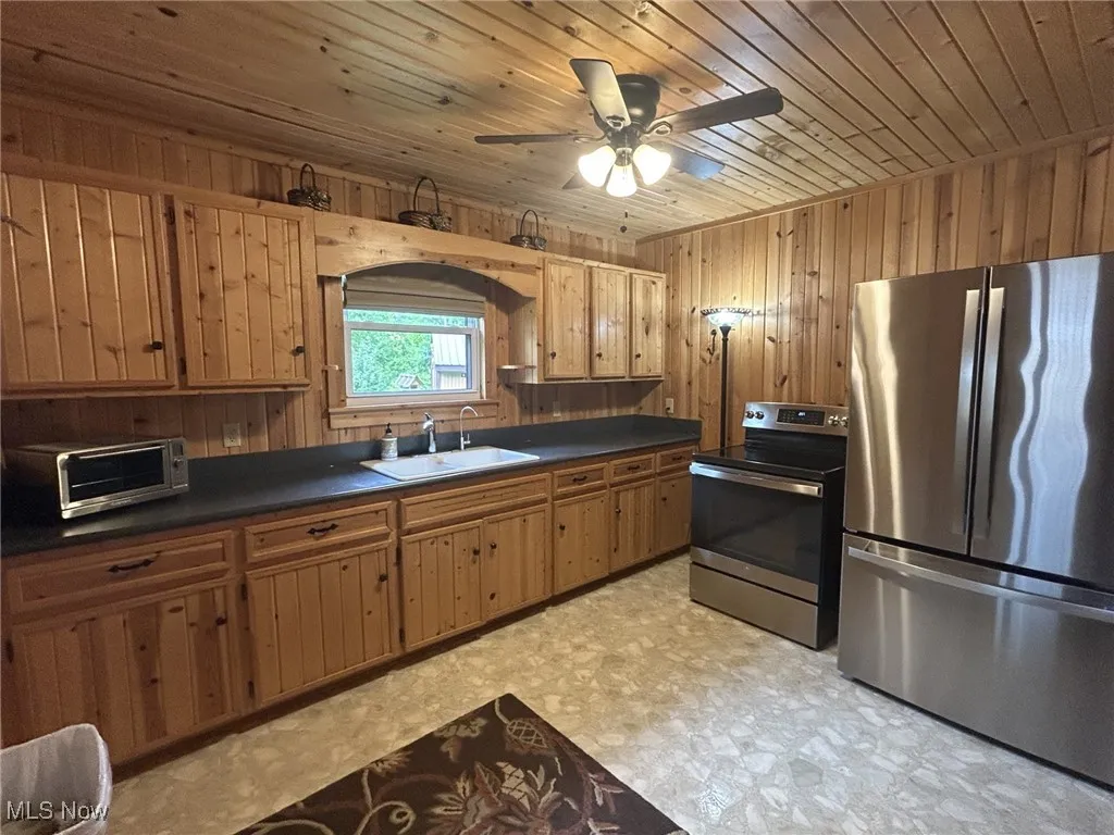 Kitchen featuring stainless steel appliances, a sink, dark countertops, light floors, and wooden walls