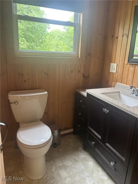 Bathroom featuring toilet, wood walls, and vanity