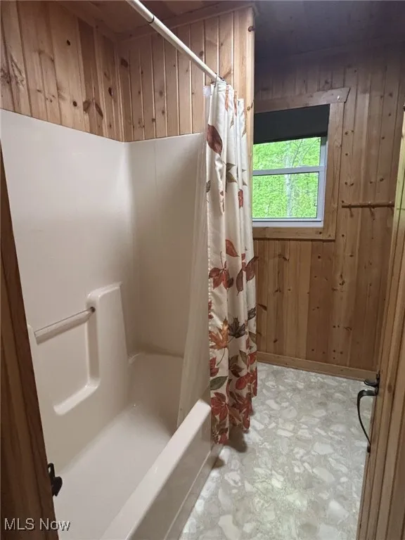 Bathroom with wooden walls and shower / bath combo with shower curtain