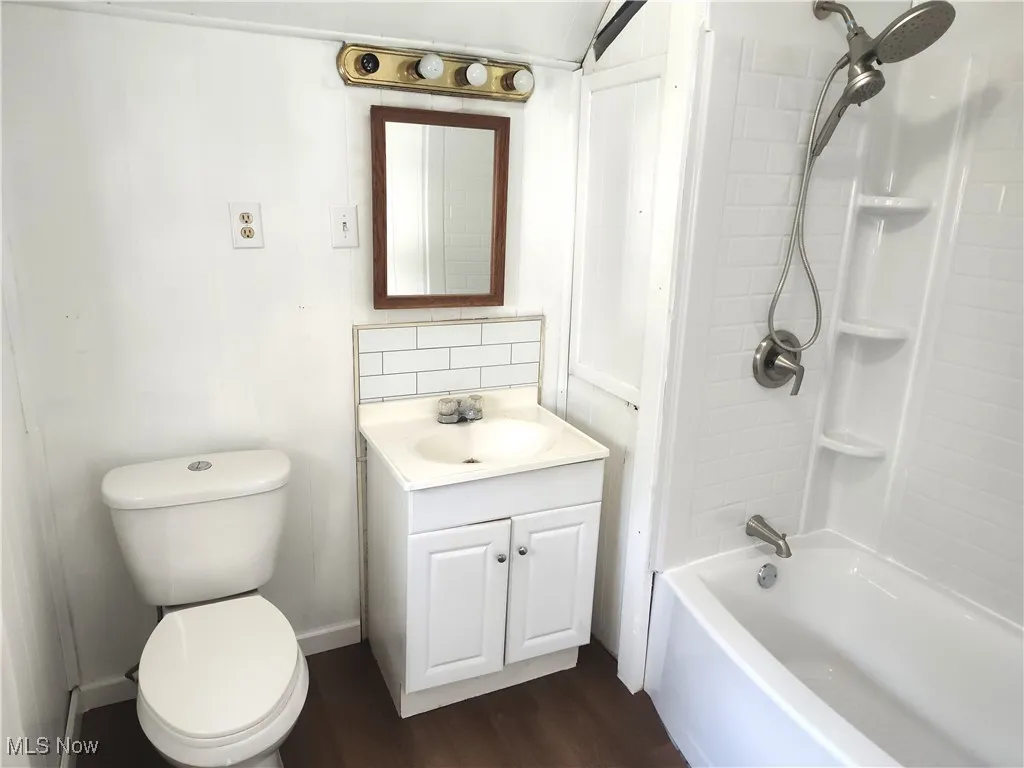 Bathroom with vanity, toilet, shower / bathtub combination, wood finished floors, and backsplash