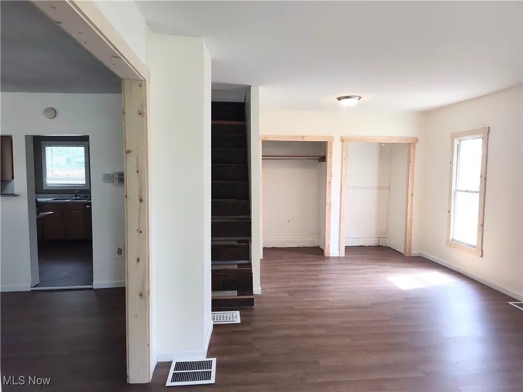 Unfurnished bedroom with two closets, wood finished floors, and baseboards