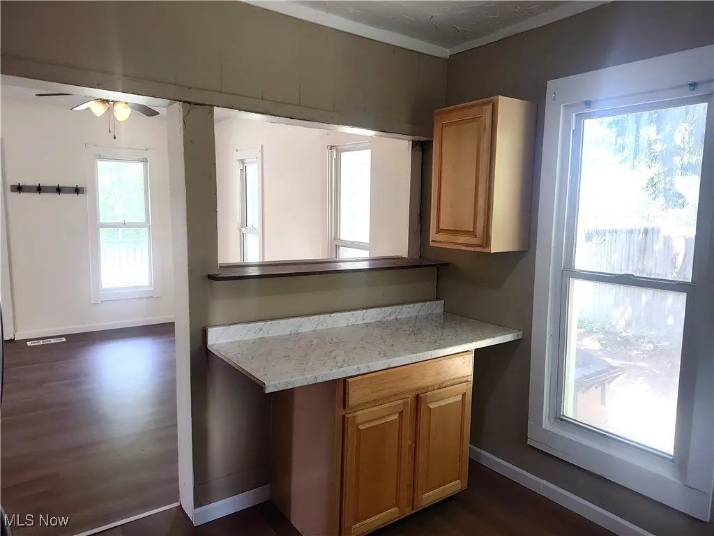 Kitchen with dark wood finished floors, ceiling fan, baseboards, crown molding, and light stone countertops