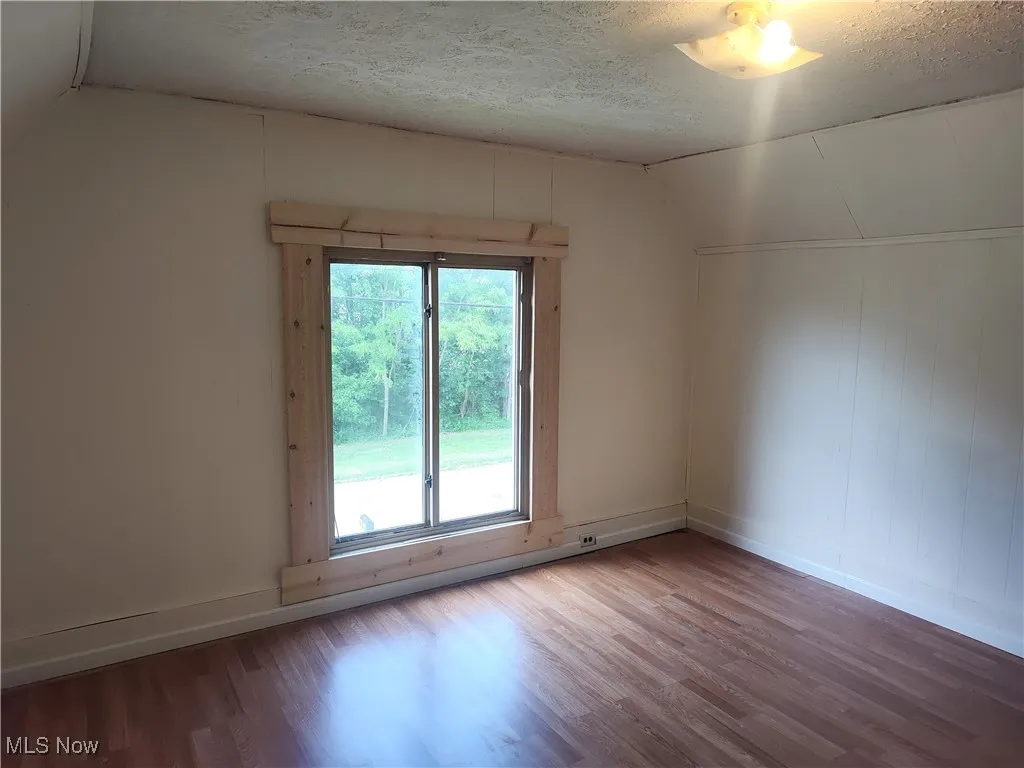 Spare room with wood finished floors, lofted ceiling, a textured ceiling, and baseboards