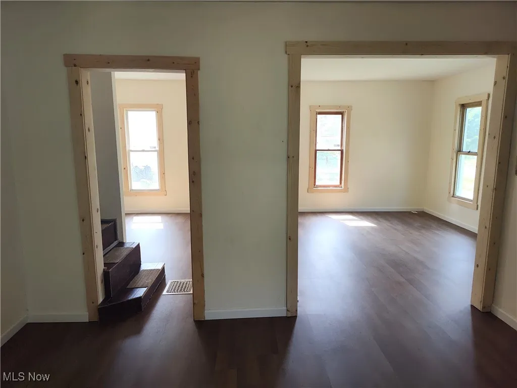 Empty room with dark wood-style flooring, healthy amount of natural light, and baseboards
