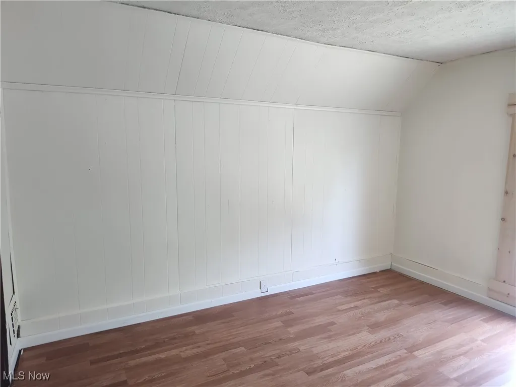Additional living space featuring wood finished floors, baseboards, lofted ceiling, and a textured ceiling