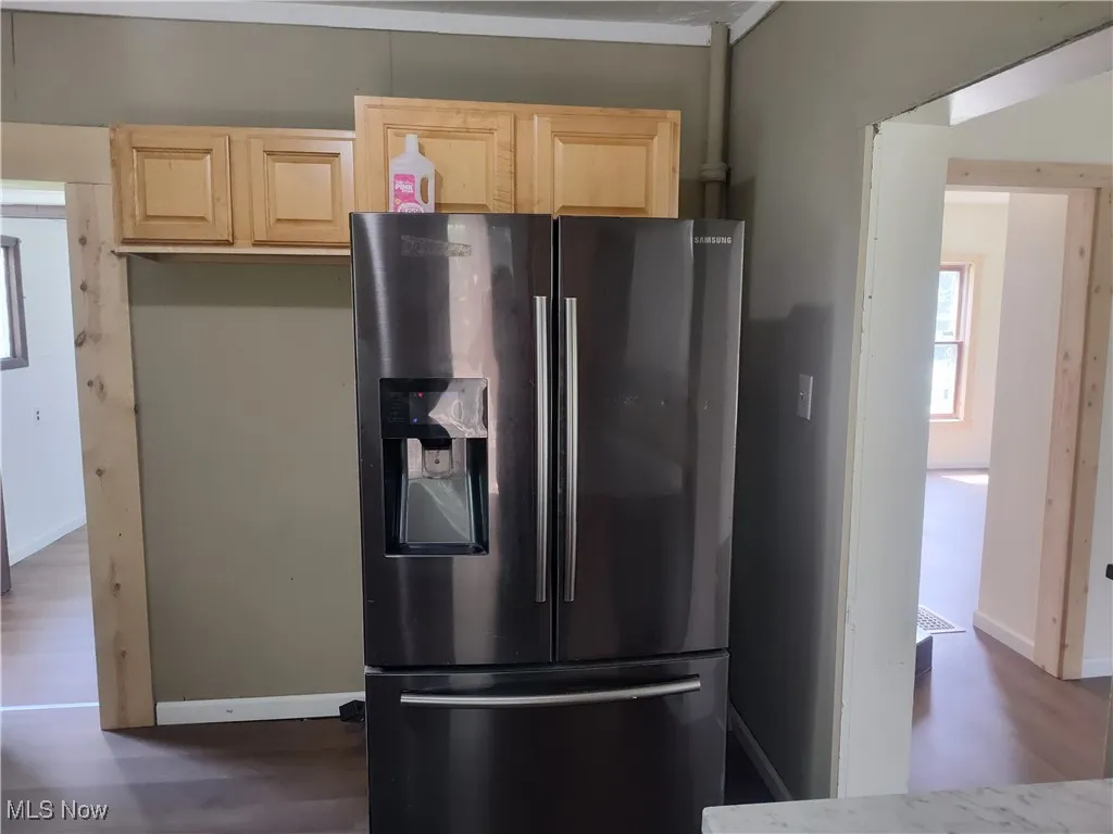 Kitchen featuring stainless steel fridge with ice dispenser, light brown cabinetry, dark wood-type flooring, and baseboards
