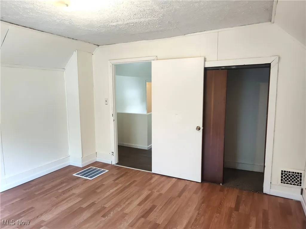 Unfurnished bedroom with wood finished floors, vaulted ceiling, a closet, a textured ceiling, and baseboards