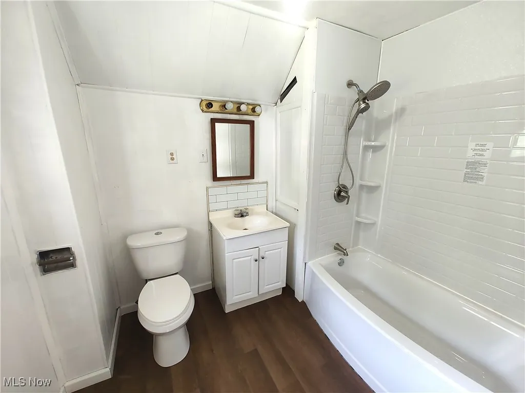 Bathroom with vanity, wood finished floors, toilet, shower / bathtub combination, and lofted ceiling