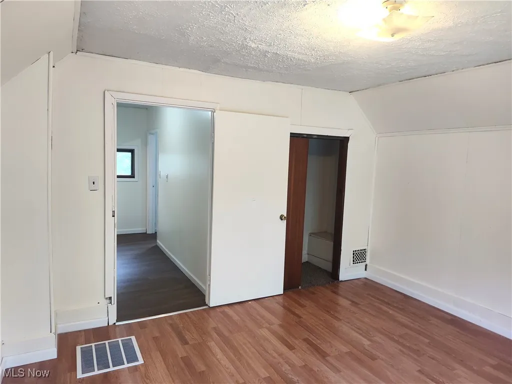 Unfurnished bedroom featuring lofted ceiling, wood finished floors, a textured ceiling, baseboards, and a closet