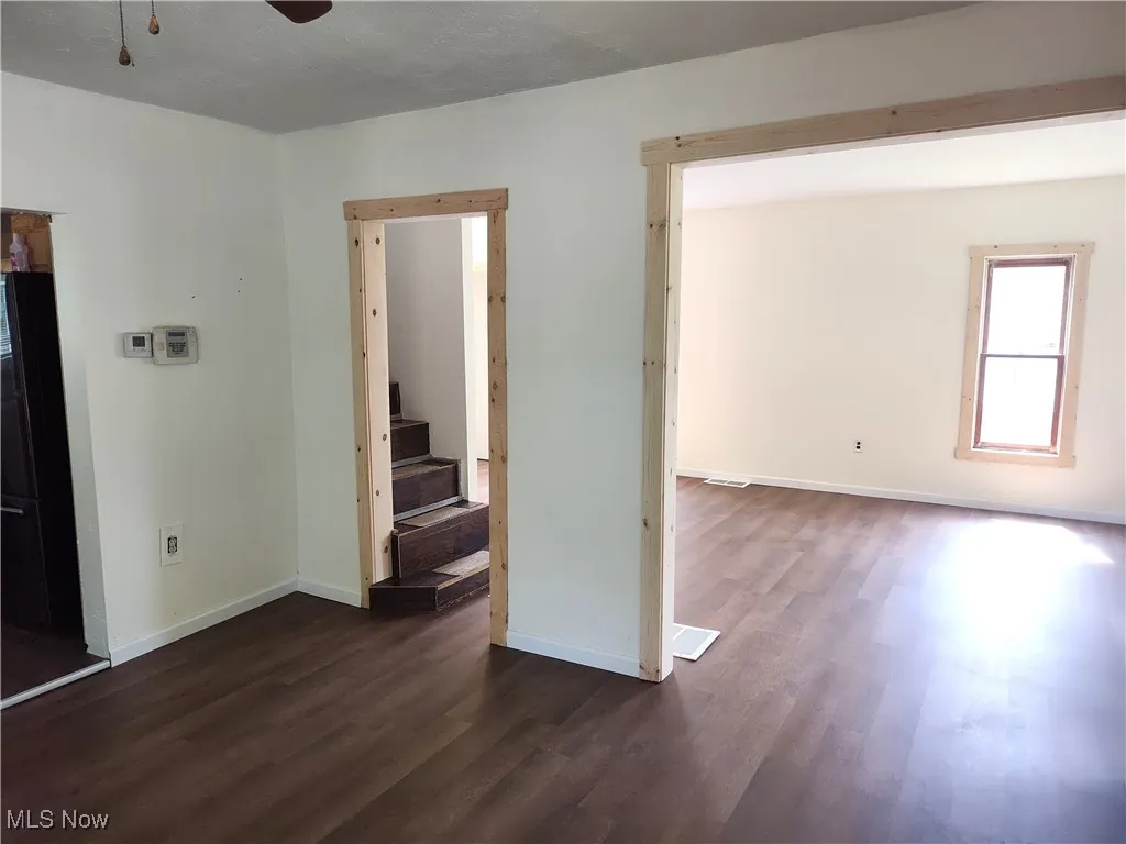 Unfurnished room featuring dark wood-style flooring, baseboards, a ceiling fan, and stairway
