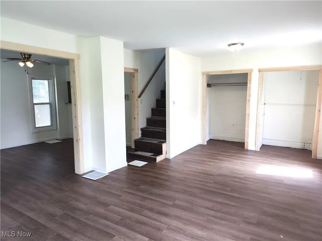 Unfurnished living room featuring stairs, dark wood finished floors, ceiling fan, and baseboards