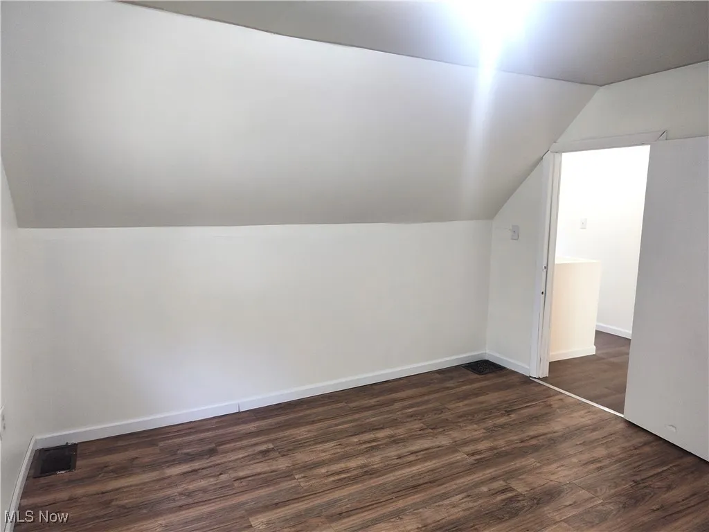 Additional living space featuring lofted ceiling, dark wood-style flooring, and baseboards