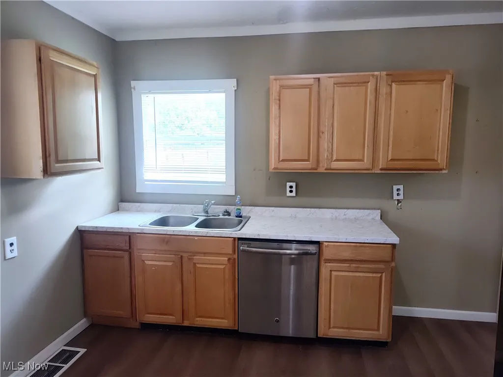 Kitchen with dishwasher, a sink, dark wood-style floors, light countertops, and baseboards