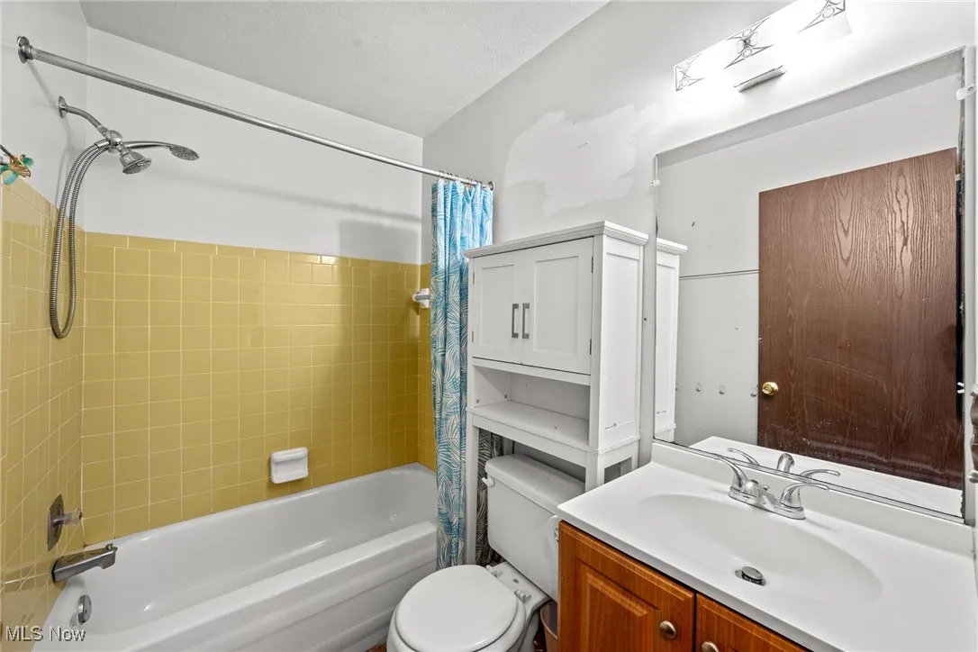 Bathroom featuring shower / bathtub combination with curtain, vanity, and toilet
