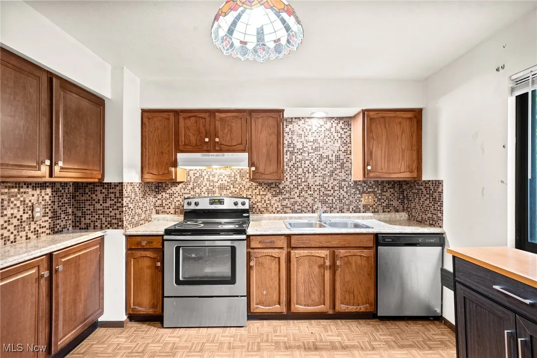 Kitchen with appliances with stainless steel finishes, a sink, under cabinet range hood, and light countertops