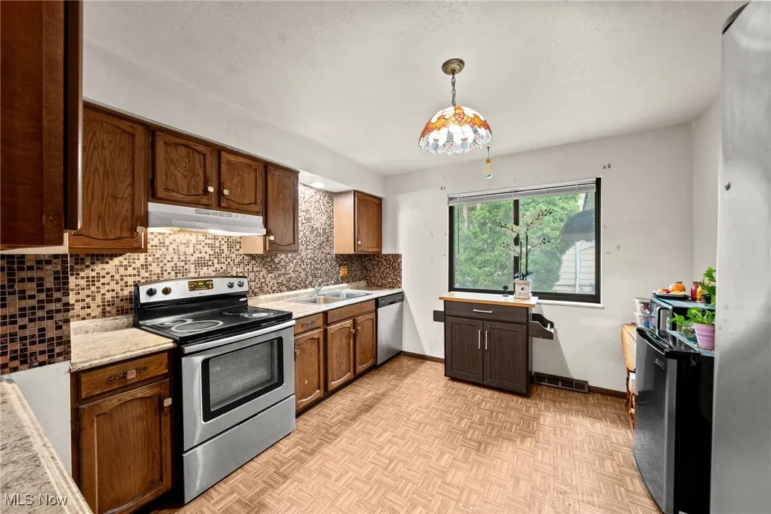 Kitchen with stainless steel appliances, under cabinet range hood, a sink, light countertops, and backsplash