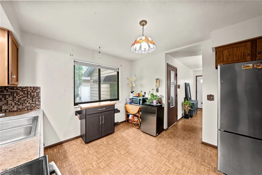 Kitchen with freestanding refrigerator, light countertops, decorative backsplash, a sink, and baseboards