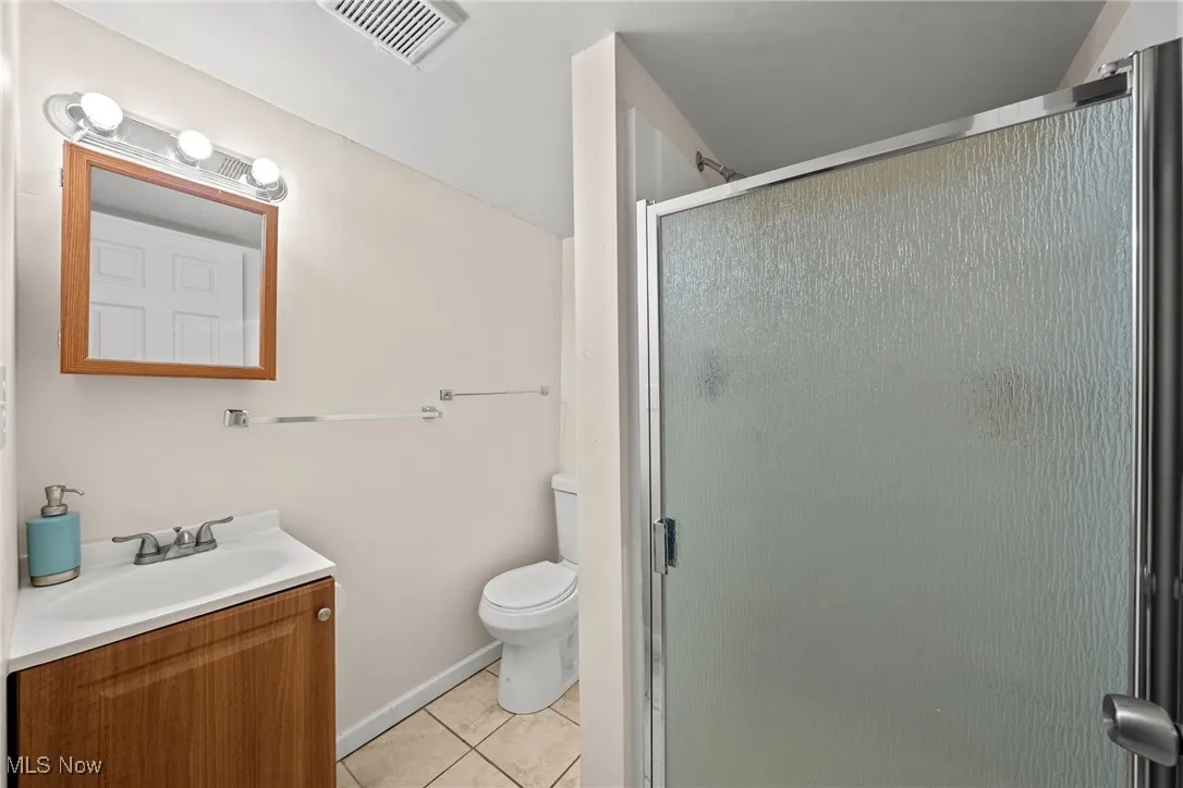 Bathroom featuring tile patterned floors, vanity, a stall shower, and toilet